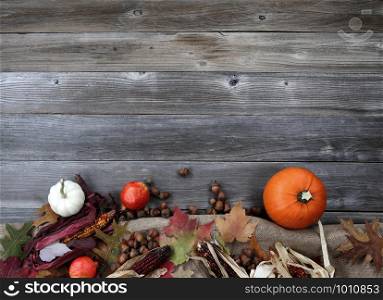 Thanksgiving Pumpkin with acorns and corn on burlap cloth forming border on weathered wood