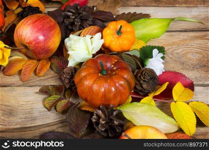 Thanksgiving rustic background with pumpkins, pine cones, apple, fall leaves and white flowers