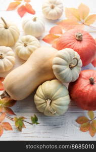 Thanksgiving season still life with small pumpkins and fall leaves over rustic wooden background