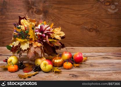Thanksgiving table centerpiece with golden leaves in vase and apples on the rustic wooden background, copy space