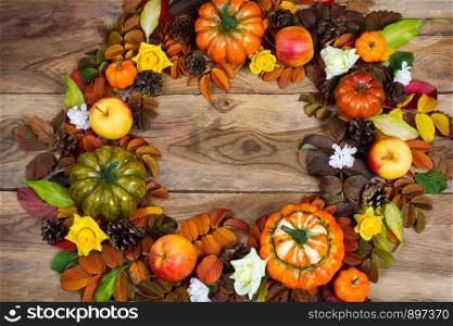 Thanksgiving wreath with pumpkins, apples, colorful fall leaves, pine cones, yellow roses and white flower wreath on the rustic wooden background