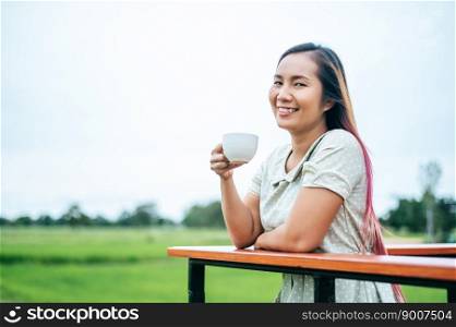 That woman stood happily drinking coffee on the meadow.