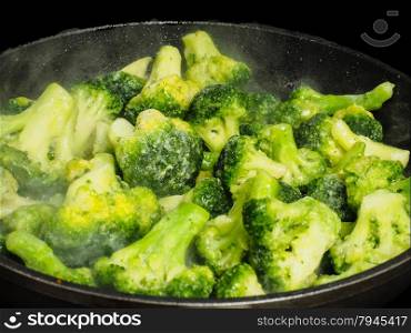 Thawing frozen green broccoli in a hot fry pan