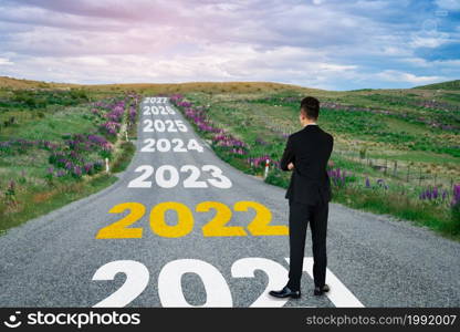 The 2022 New Year journey and future vision concept . Businessman traveling on highway road leading forward to happy new year celebration in beginning of 2021 for fresh and successful start .. The 2022 New Year journey and future vision concept