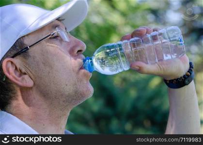 The 50s age man is drinking bottle of water during the walk.