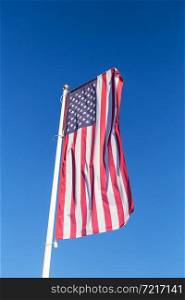 The American flag flies against a clear blue sky, vertical. Freedom and independence concept. The American flag flies against a clear blue sky, vertical. Freedom and independence concept.