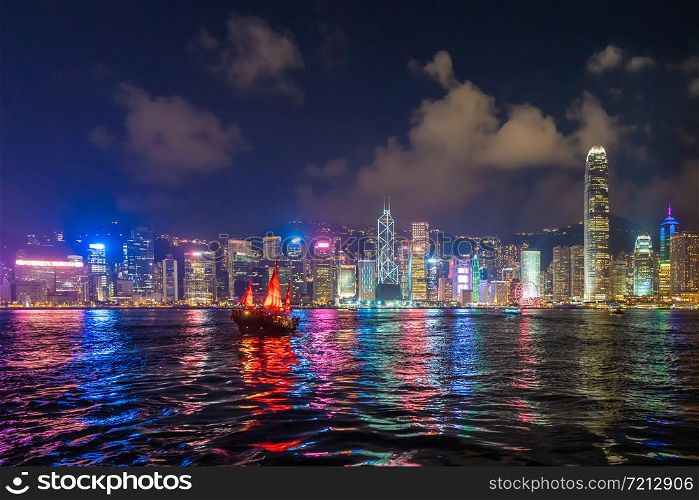 The Aqua Luna sailing in Hong Kong Downtown with skyscraper buildings. financial district in urban city at night. The red boat or ship is a Chinese Junk operating in Victoria Harbour.