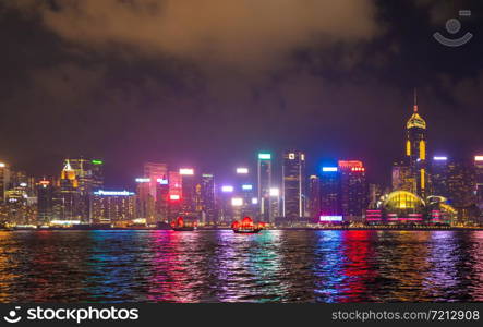 The Aqua Luna sailing in Hong Kong Downtown with skyscraper buildings. financial district in urban city at night. The red boat or ship is a Chinese Junk operating in Victoria Harbour.