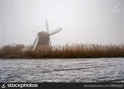 The archetypal Dutch winter on a foggy morning on a frozen canal surrounded by reed, and a windmill