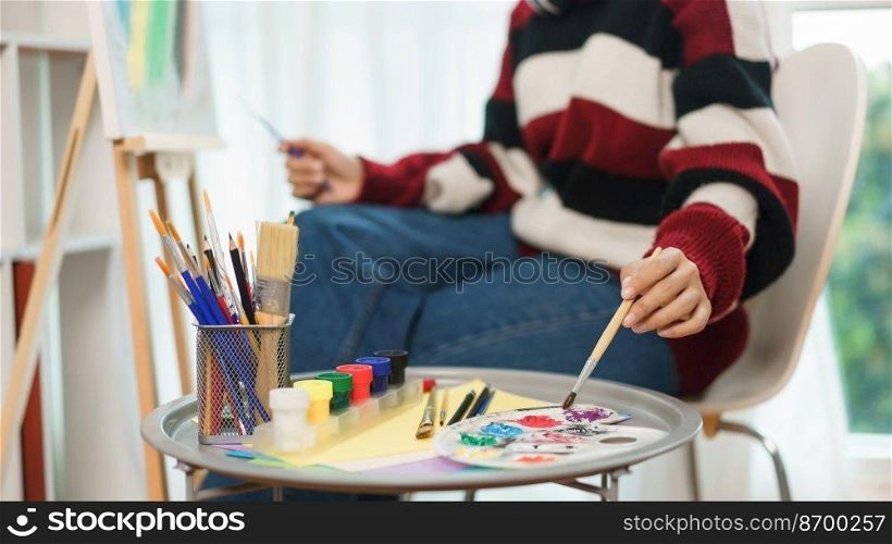 The art concept, Asian female artist smiling to happy while using brush to dip in color palette.
