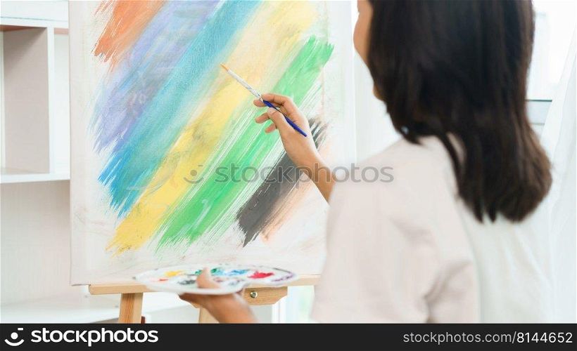 The art concept, Asian female artist using paintbrush to create masterpiece on canvas in art studio.