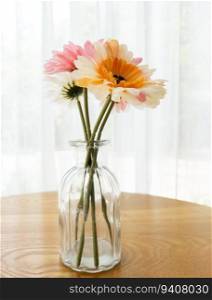 The artificial flower in the clear glass vase on the wooden table near the window for decorated in the coffee cafe, front view with the copy space.