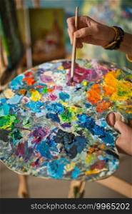 The artist holds a palette in her hand and mixes colors.. A huge palette in the hands of the artist at work 2875.