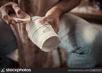 the artist polishing rough edges of a ceramic pot with a sponge in pottery studio.  . the artist polishing rough edges of a ceramic pot with a sponge