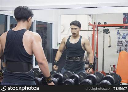 The asian sportsman stand in front of the mirror in the gym