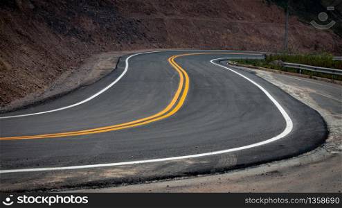 The asphalt road has yellow and white traffic lines crossing the mountains.