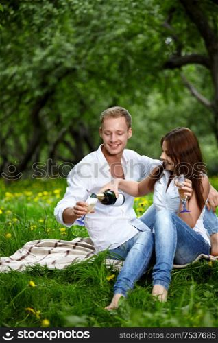 The attractive enamoured couple drinks champagne in park
