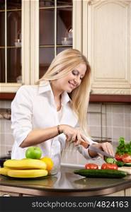 The attractive girl cuts vegetables on kitchen