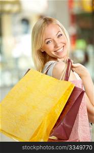 The attractive girl looks and smiles through a shoulder, holding in hands multi-coloured bags with purchases