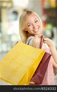 The attractive girl looks and smiles through a shoulder, holding in hands multi-coloured bags with purchases. Good shopping!