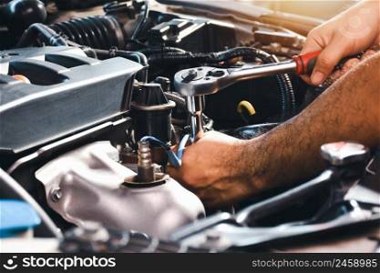 The auto mechanic is fixing the engine of the car with a socket wrench
