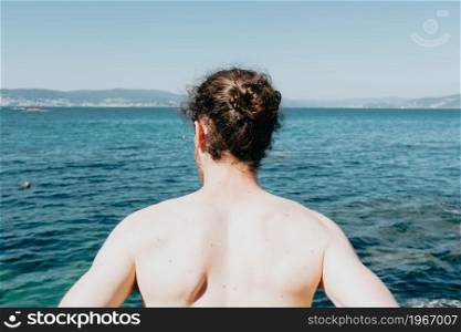 The back of a young man in front of the ocean during a sunny day with confidence, liberty and future concepts, copy space, summer, holiday