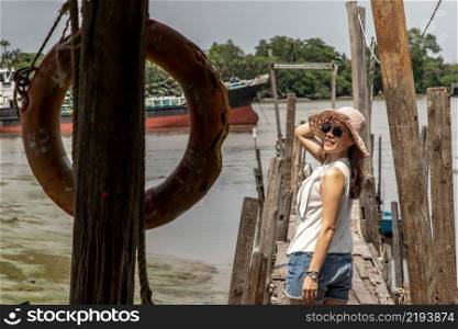 The back of a young woman in casual clothes standing on an old wooden pier and looking at the view Chao Phraya River the afternoon. Personal holiday.