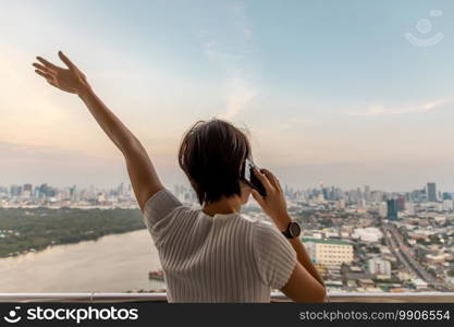 The back of young woman happy talking cell phone while standing on the balcony with against city view of bangkok. Copy space, Selective focus.