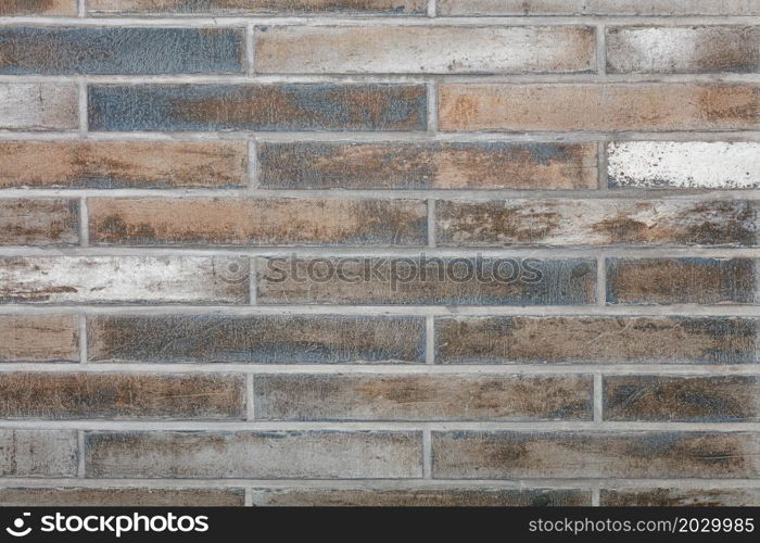 The background and texture of the wall is lined with old rough tiles with scratches, faded spots in gray, green and brown tones in a retro style.. The wall is faced with old oblong rough tiles in horizontal design. Wall texture with smooth cement joints.