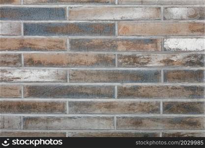 The background and texture of the wall is lined with old rough tiles with scratches, faded spots in gray, green and brown tones in a retro style.. The wall is faced with old oblong rough tiles in horizontal design. Wall texture with smooth cement joints.