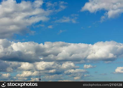 The background and texture of white fluffy clouds float in a rhythmic row high in the sky and cling to the top of the television tower?s spire. Copy space.. Lush white clouds cling to the top of the television tower?s spire high above the blue sky.