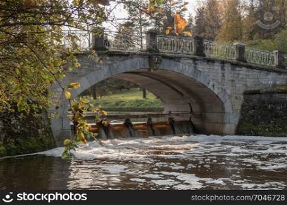 The bank of the autumn river with a stone arch bridge
