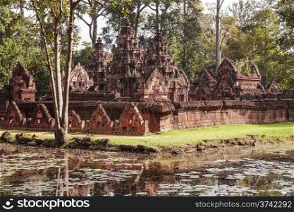 The Banteay Srei temple is one of the oldest temples in the Angkor Wat area of Cambodia. As viewed from the outside over a pond, the well-preserved building was made of a reddish stone.