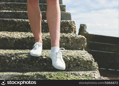 The bare legs of a young woman as she is walking down some steps on the beach