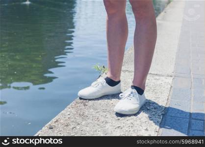The bare legs of a young woman standing by a canal