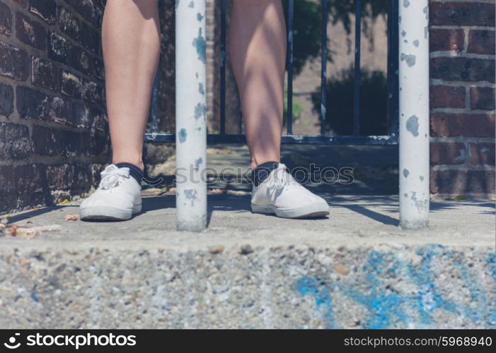 The bare legs of a young woman standing by some bars outside