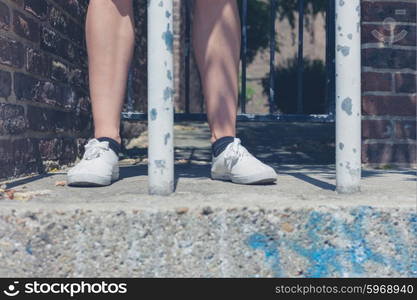 The bare legs of a young woman standing by some bars outside