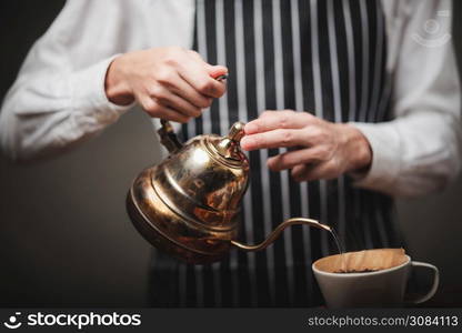 The barista poured hot water from the kettle over the coffee powder to extract the freshly brewed coffee in the coffee shop.