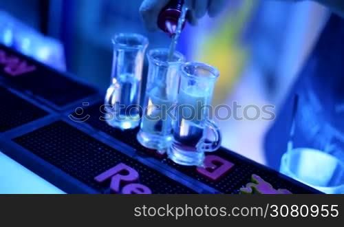 The barman makes a cocktail-shot. A man is preparing a drink. Alcohol. A party. A young man is working at a bar counter.
