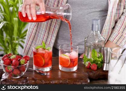 The bartender prepares a refreshing strawberry mojito cocktail with ice, fresh mint and lime. Great idea for a picnic or summer party. It may contain alcohol or be a mocktail.