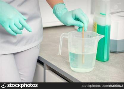 The beautician uses a stick to mix disinfectant into the water. Sterilization of tools. The beautician uses a stick to mix disinfectant into the water. Sterilization of tools.