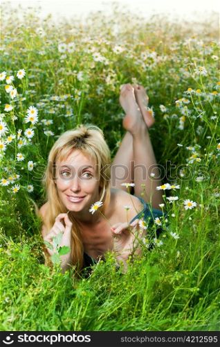 The beautiful happy girl lies in the field of camomiles and guesses on a camomile