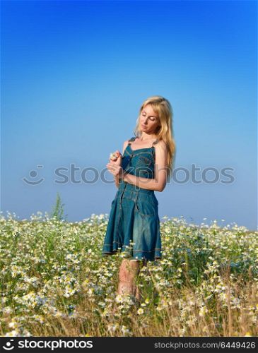 The beautiful happy young woman in the field of chamomiles guesses on a chamomile