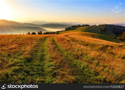 The beautiful landscape of the Carpathians in the early morning at dawn and the road that runs along the ridge of a mountain hill, creeping fog, floods with golden sunlight.. The mountain peaks of the Carpathian hills are filled with golden light in the morning sun.