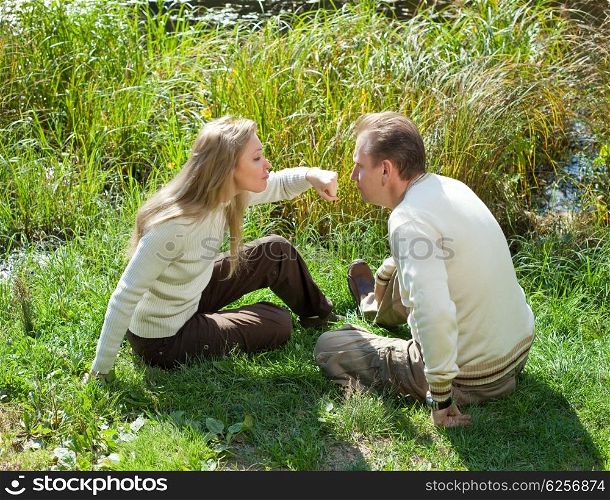 The beautiful woman for fun threatens to knock the man on a nose in the summer on a grass at the lake