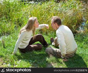 The beautiful woman for fun threatens to knock the man on a nose in the summer on a grass at the lake