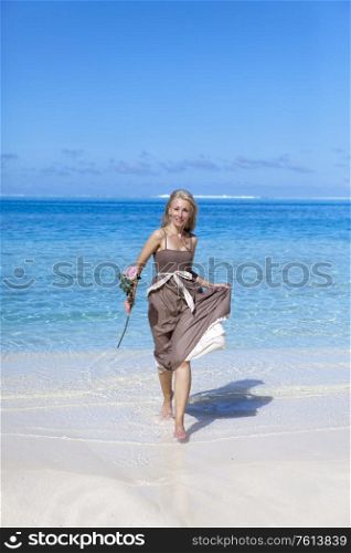 The beautiful woman with a rose runs on the edge of the sea on a beach. Polynesia.