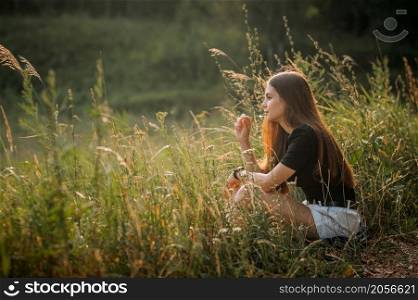 The beauty sits in the summer among the grass in the meadow.. Summer photo of a girl on the background of a grass meadow 3656.