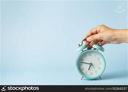 The bell alarm clock is turned off by hand against blue background for the concept of time management.