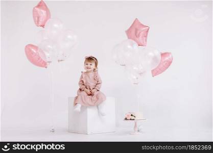 the birthday 2 years old little girl in pink dress. white cake with candles and roses. Birthday decorations with white and pink color balloons and confetti for party on a white wall. Happy birthday.. the birthday 2 years old little girl in pink dress. white cake with candles and roses. Birthday decorations with white and pink color balloons and confetti for party on a white wall. Happy birthday